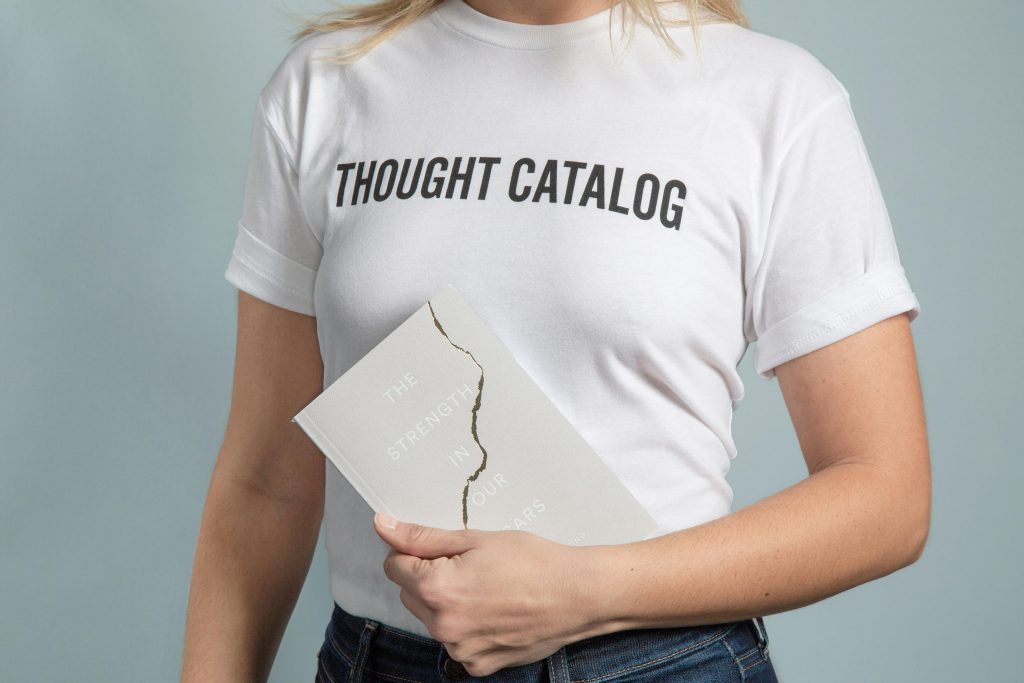 A woman wearing a white t-shirt holds a book with a cracked cover.